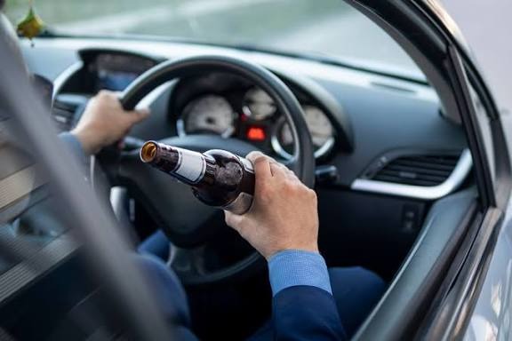 Image of a hand driving a car with a bottle of alcohol illustrating how DUI Affect Your Credit Score