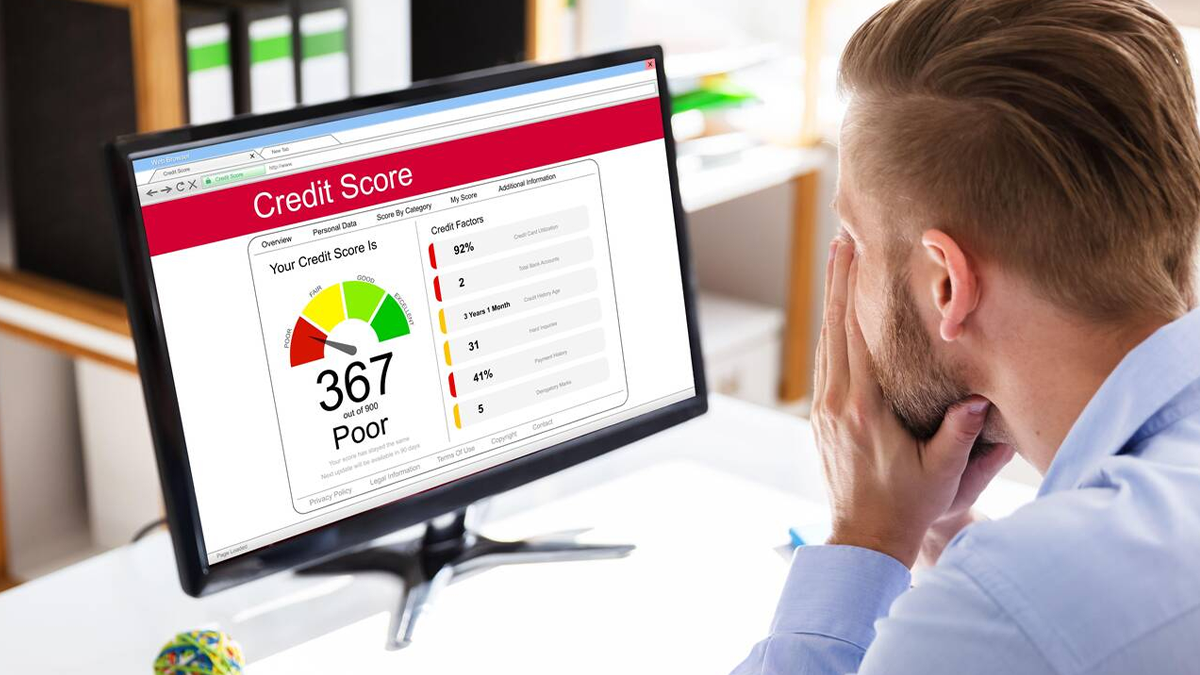 Man expressing worry and shock from the poor credit score he's viewing on his PC due to his debt collections