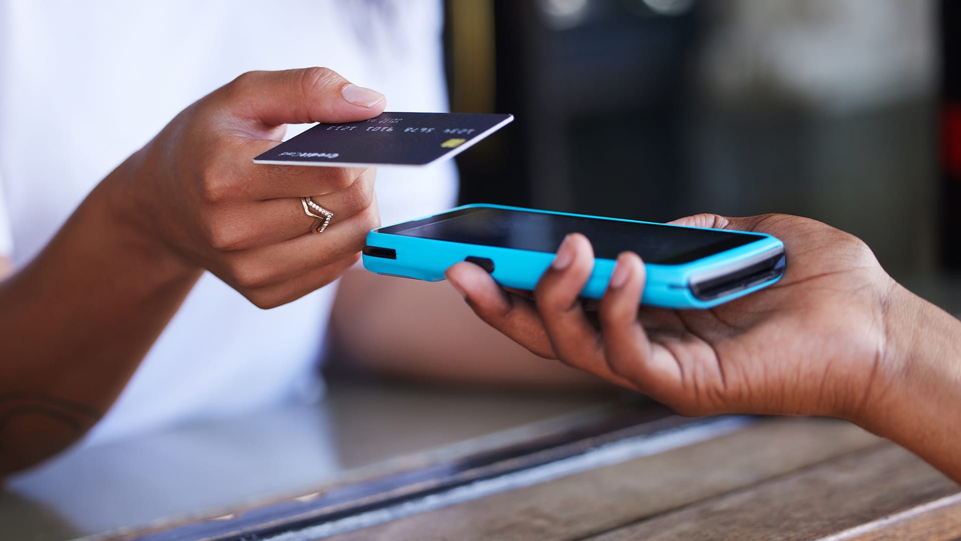 A hand passing over a credit card to another person's hand receiving it with a card machine.